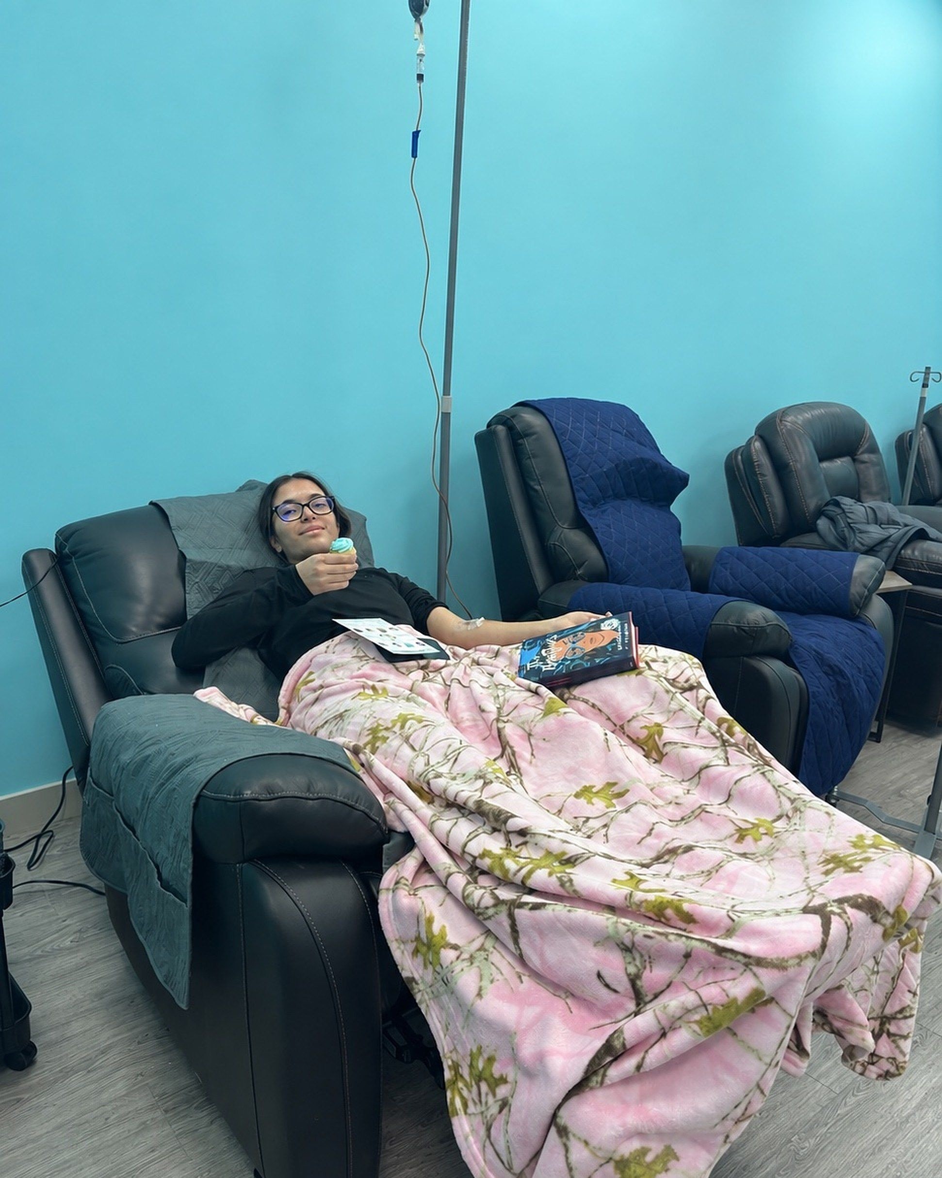 A person resting in a recliner with a blanket and a book during an infusion at Solis Medical Clinic
