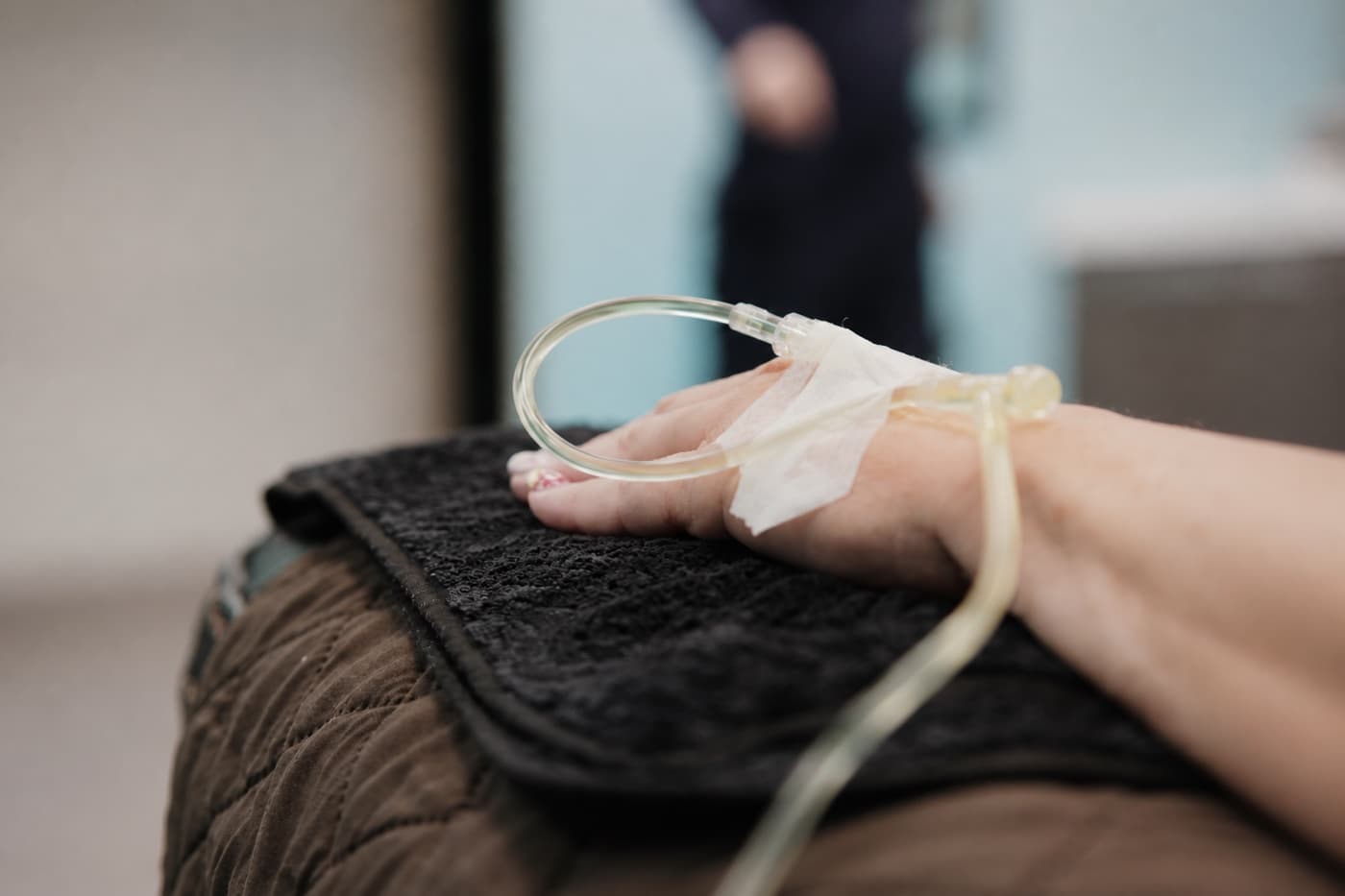 A patient's hand with an IV line taped in place during a prescription infusion at Solis Medical Clinic in Edmonton.