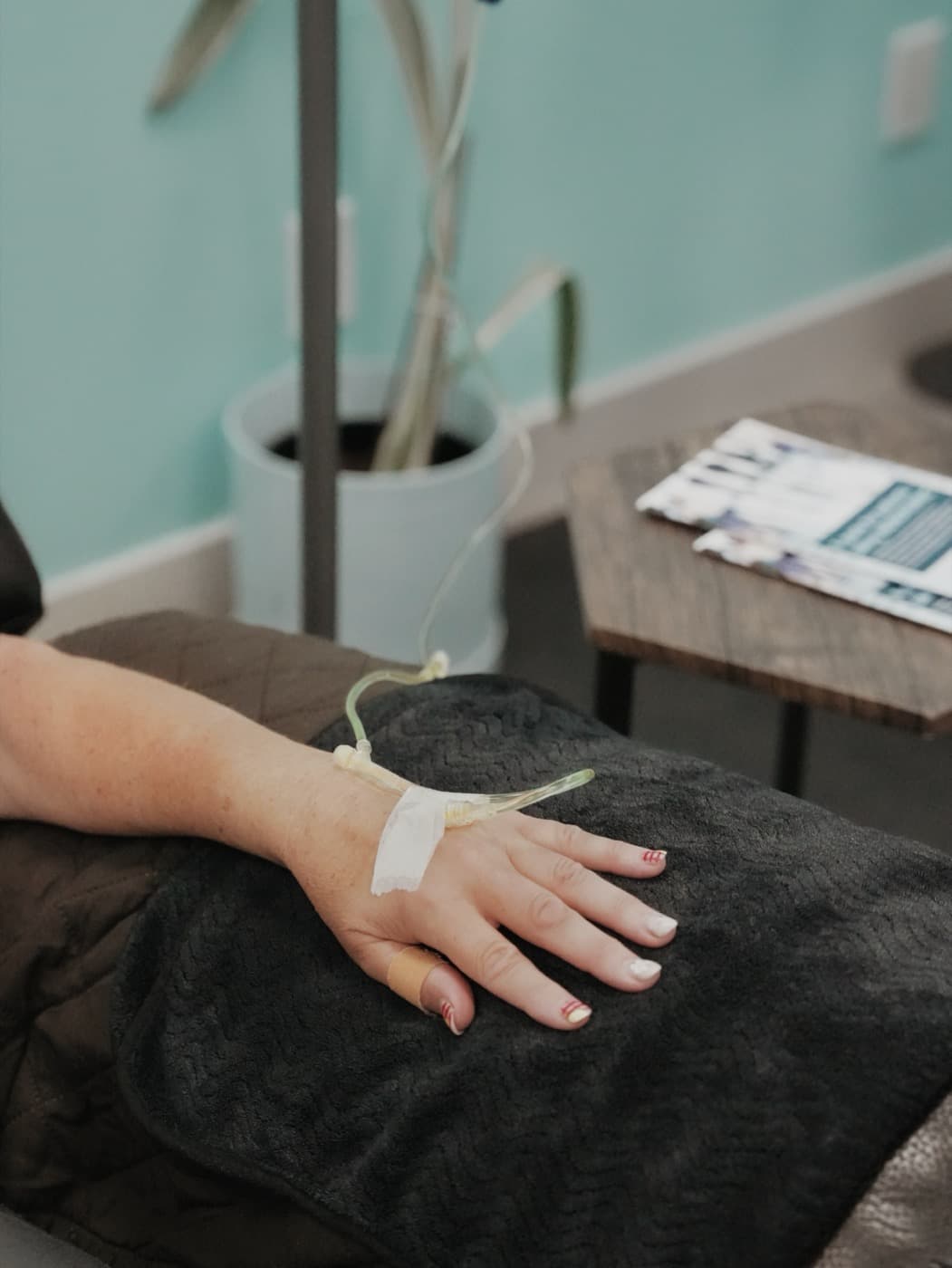 A patient resting under a blanket with an IV line taped to the back of their hand during an infusion at Solis Medical Clinic in Edmonton.